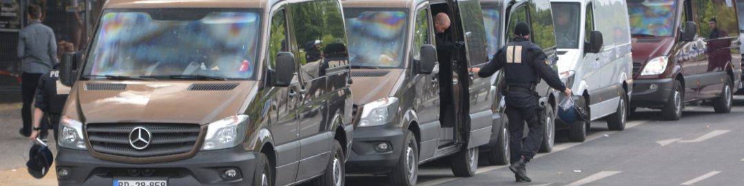 mehrer schwarze Mercedes-Transporter mit Blaulicht in einer Reihe am Straßenrand, aus dem zweiten von vorn steigen 2 Cops in schwarzem Einsatzanzug aus