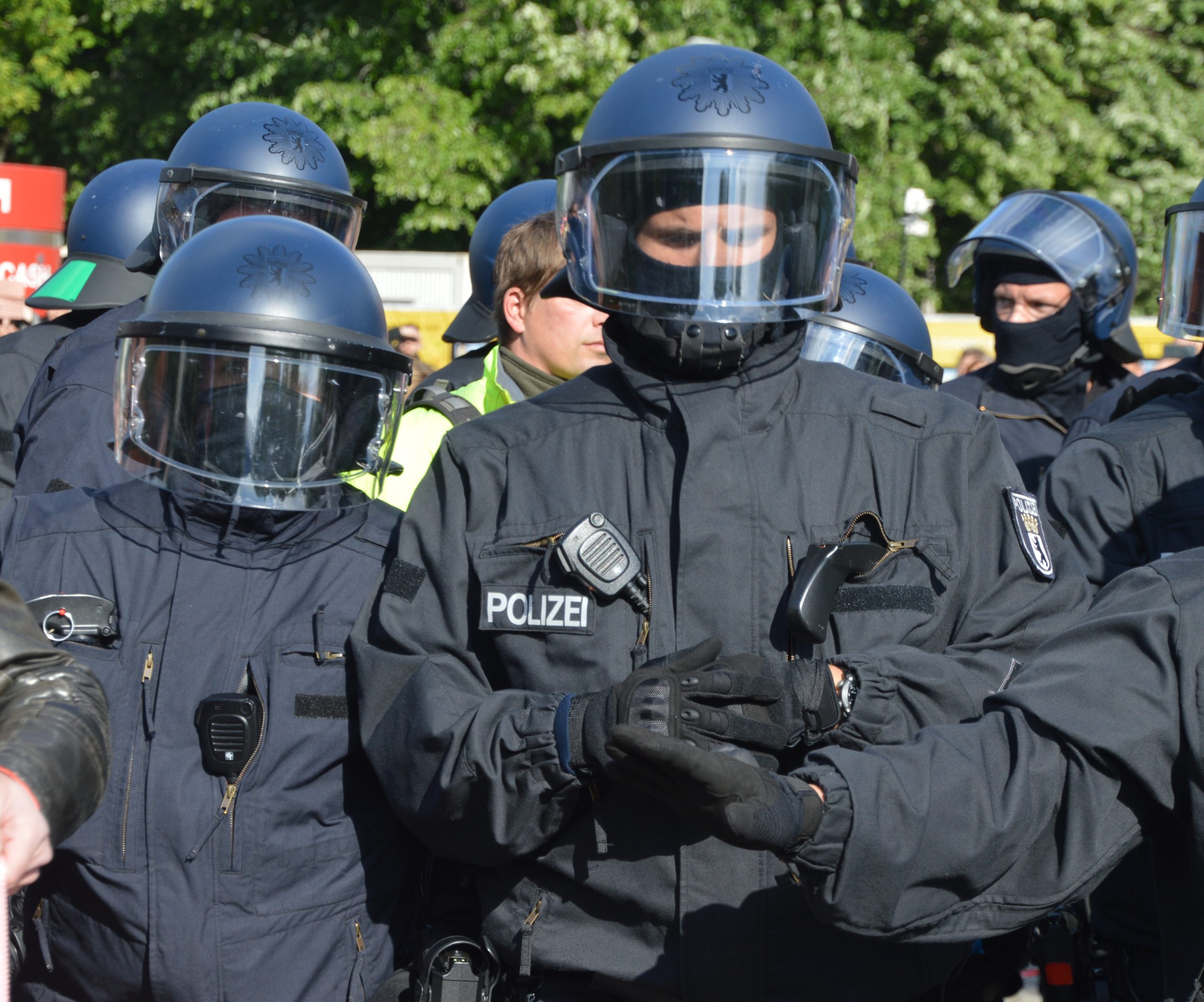 Mehrere Bullen in Riot-Ausrüstung mit Helm und heruntergelassenem Visier, sowie Funkgerät und Reizstoffgerät/Pfeffer
