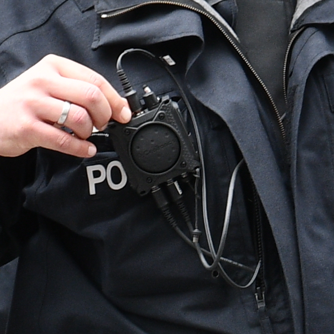 Kleines Funkgerät ist an der Brust eines Cops befestigt. Eine Hand drückt einen Knopf.